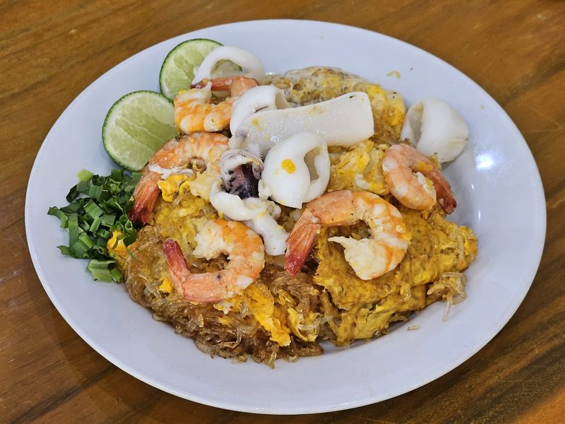 ผัดไทยวุ้นเส้นใส่กุ้งและหมึก วางมะนาวและผักข้างจาน