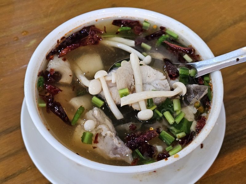 ต้มยำปลาในชามขาว ใส่เห็ด พริกแห้ง และต้นหอม