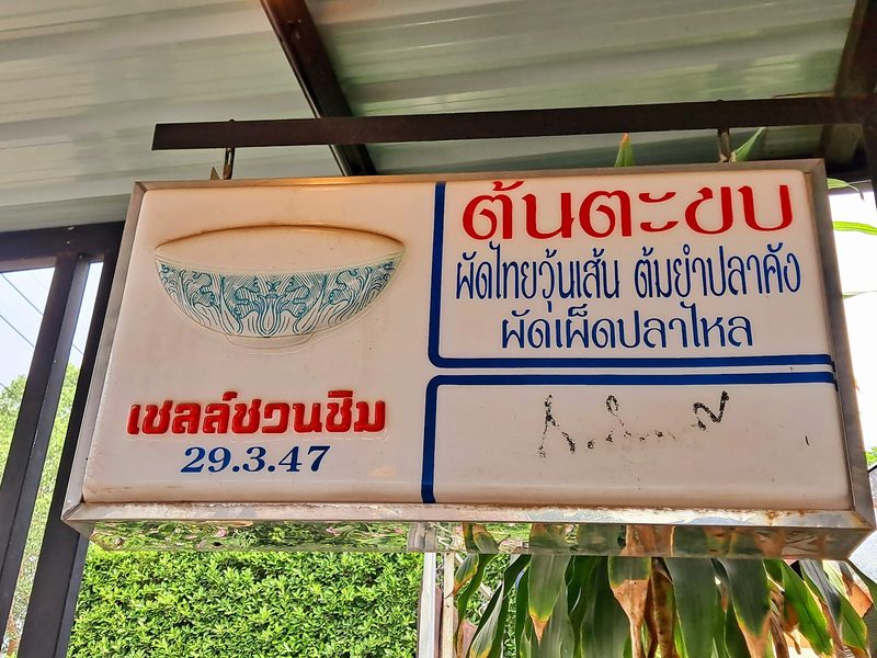 ป้ายร้านต้นตะขบ เขียนผัดไทยวุ้นเส้น ต้มยำปลาคัง ผัดเผ็ดปลาไหล และตราเชลล์ชวนชิม