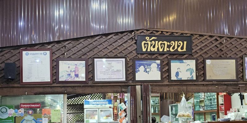 ในร้านต้นตะขบ ป้ายชื่อร้านเหนือช่องครัว ผนังระแนงไม้ติดรูปถ่ายและกรอบเกียรติบัตร